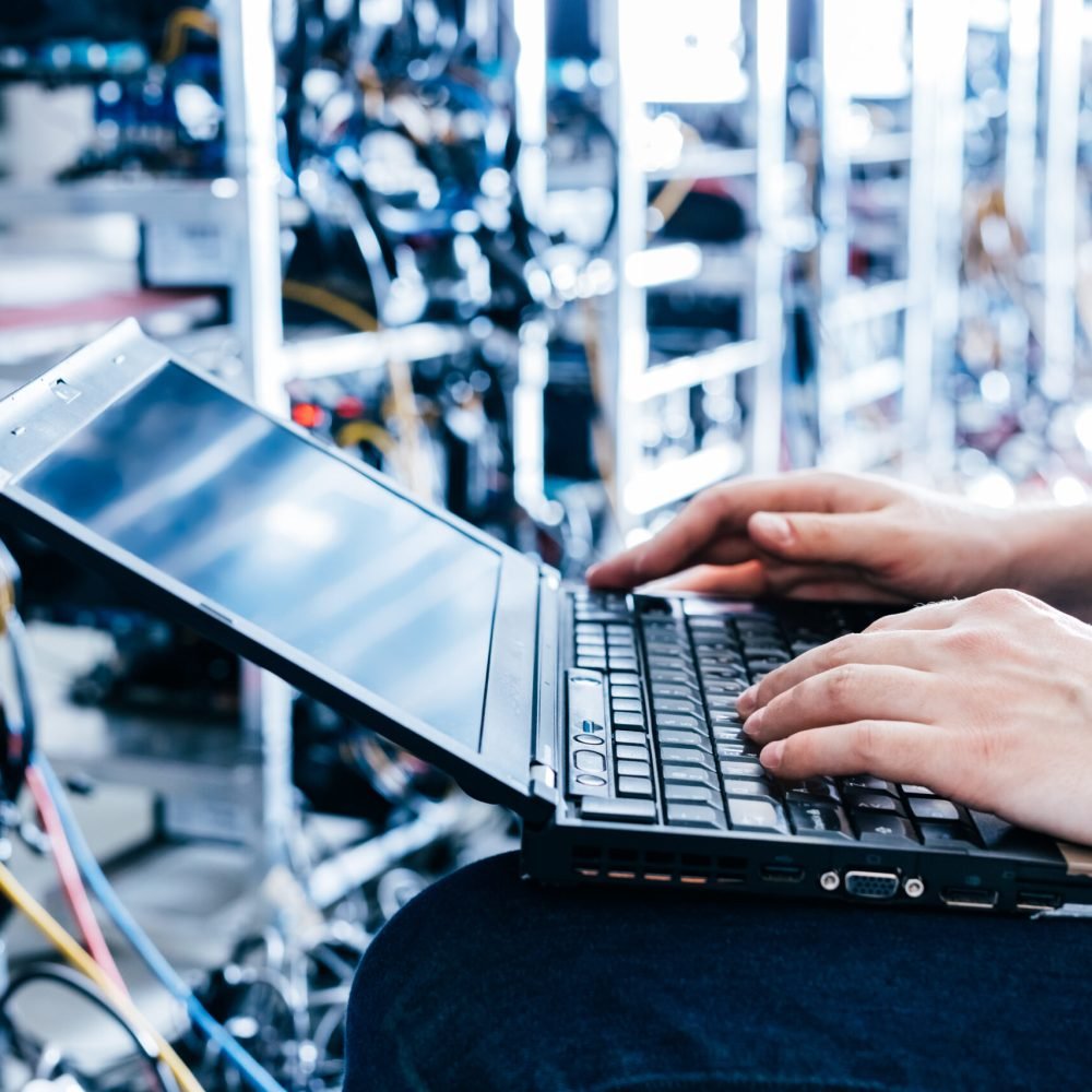 IT specialist working on computer in bitcoin and crypto currency mining farm. Big data center. High tech server computers at work