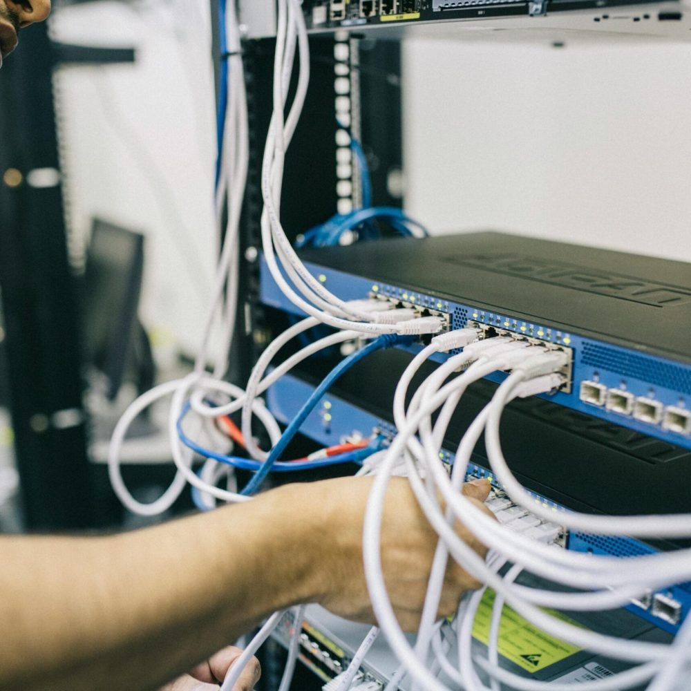 An IT professional configuring network cables in a server rack, focusing on Ethernet connections.